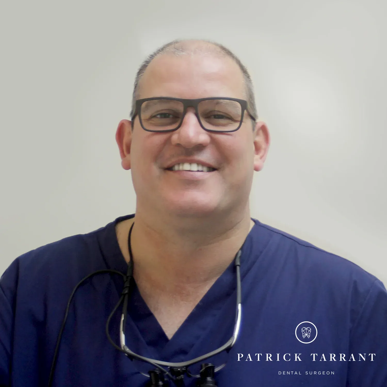Dr Patrick Tarrant, Dental Surgeon, in navy scrubs with loupes around his neck